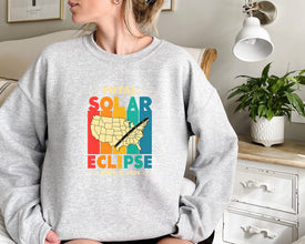 a woman sitting on a couch wearing a sweatshirt that says solar eclipse