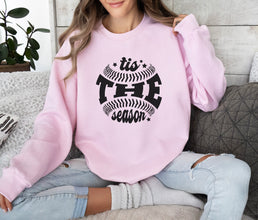 a woman sitting on a couch wearing a pink sweatshirt