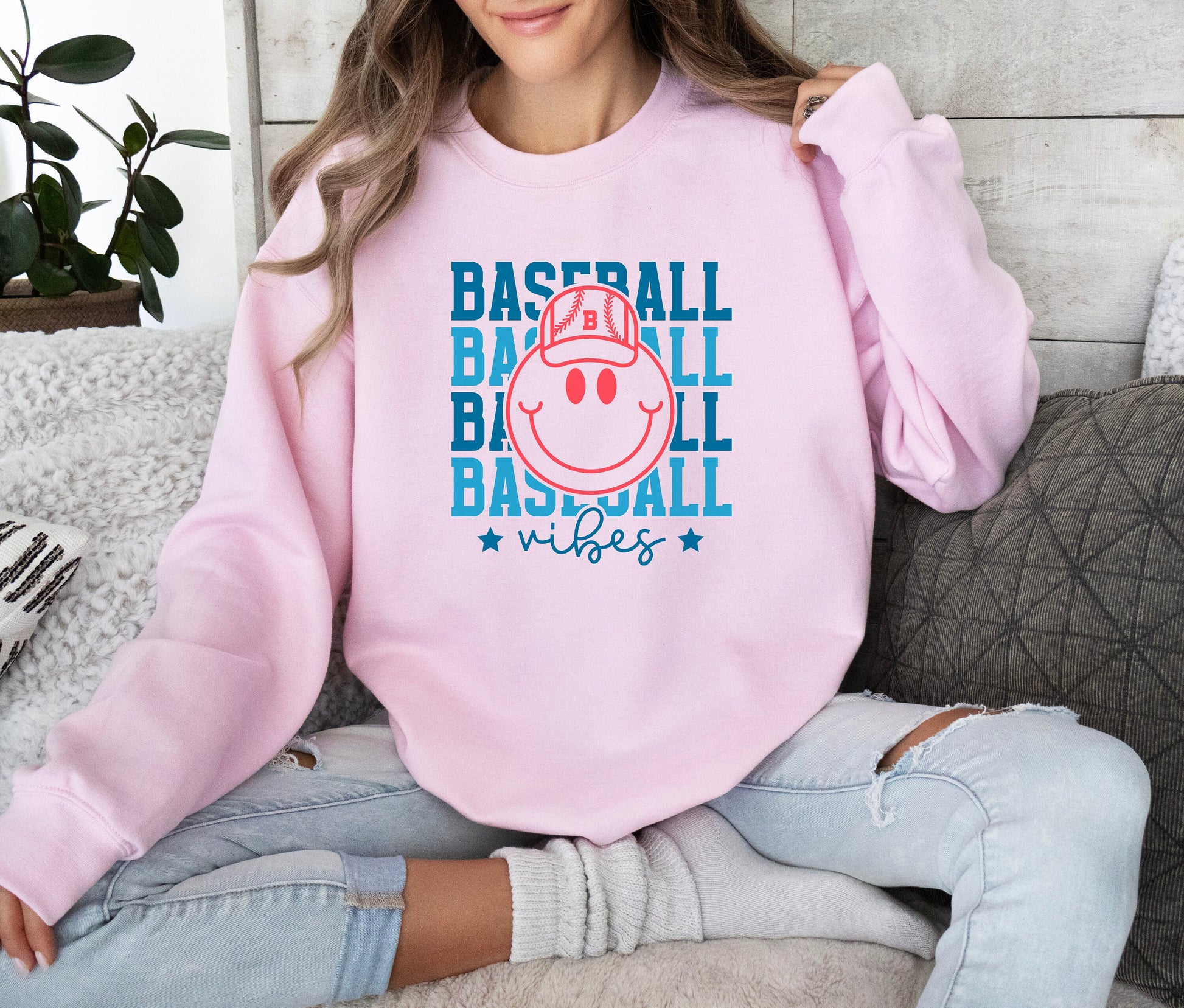 a woman sitting on a couch wearing a pink baseball sweatshirt