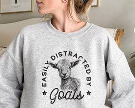 a woman sitting on a couch wearing a sweatshirt that says easily distracted by goats