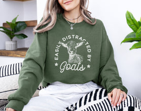 a woman sitting on a couch wearing a sweatshirt with a goat on it