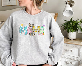 a woman sitting on a couch wearing a sweatshirt that says mama